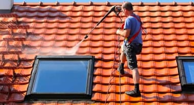 Person pressure washing a roof with sky light windows