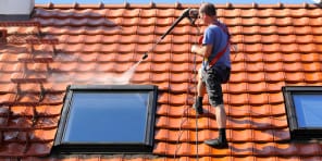 person pressure washing a roof with sky light windows